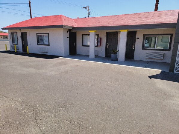 Un motel con techo rojo, estacionamiento y un pequeño jardín.