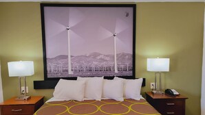 A hotel room with a bed, two bedside tables, a nightstand, a lamp, a framed picture of wind turbines, and a wall-mounted phone. - Super 8 By Wyndham El Centro North (El Centro)