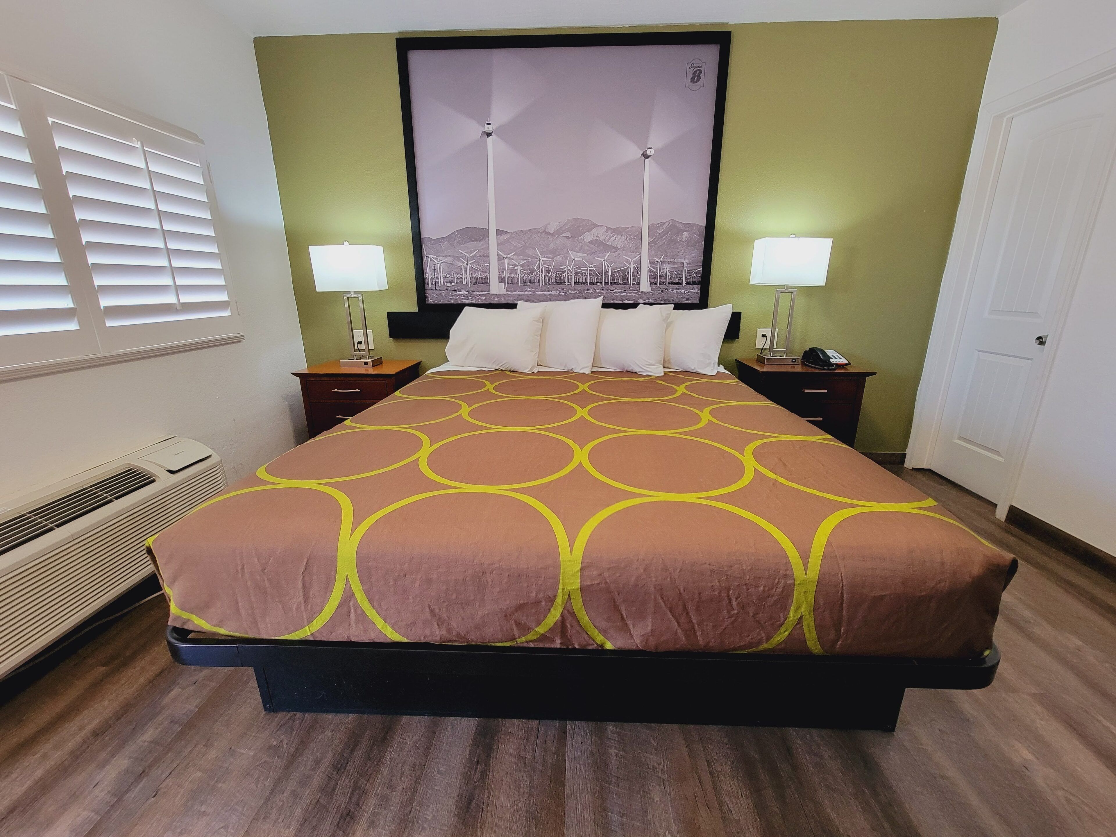 A hotel room with a bed, two bedside tables, a wall-mounted TV, and a window with blinds.