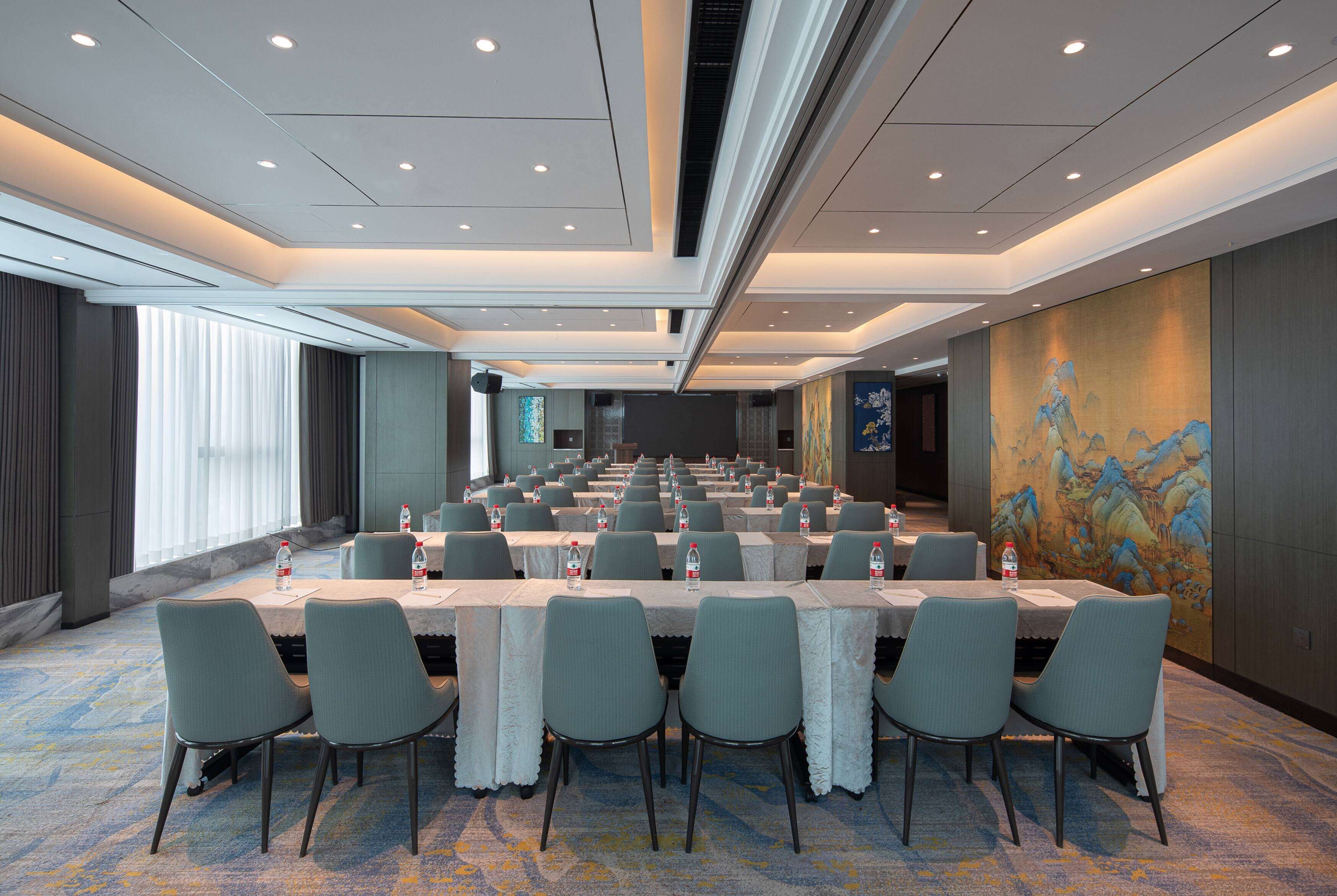 Un salón de conferencias con varias mesas y sillas, equipado con botellas de agua, en un moderno hotel.