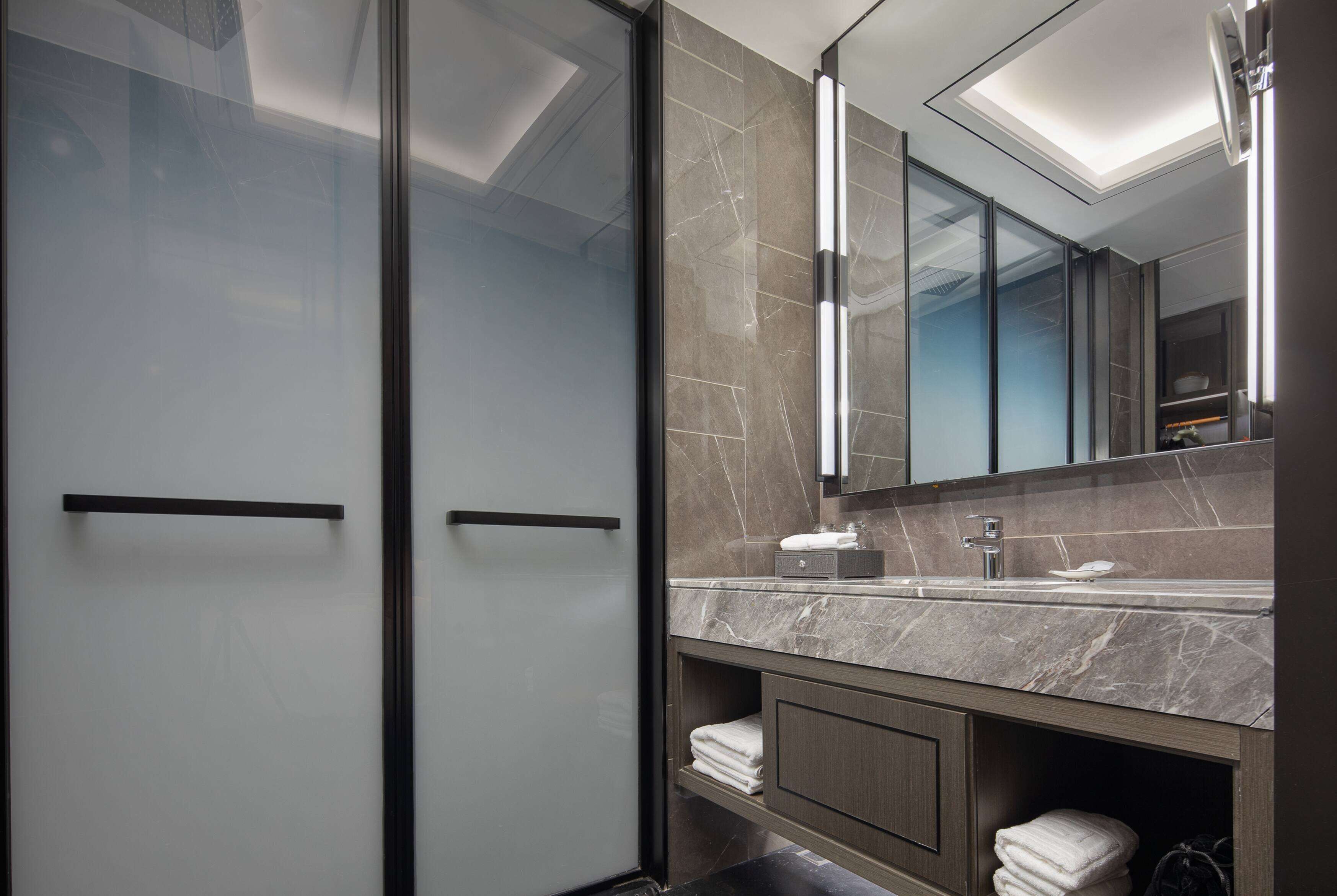 A modern bathroom with a glass shower enclosure, a marble sink, and a large mirror.