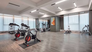 Un gimnasio espacioso con diversos equipos de ejercicio, ventanas amplias y un diseño moderno en el techo.