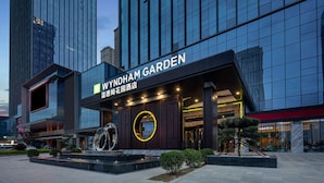 Una entrada de hotel moderna con un letrero destacado, un elemento decorativo circular y un área ajardinada con un pequeño árbol.
