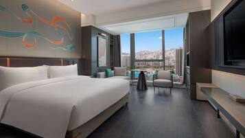 A modern hotel room with a large bed, a TV, and a view of the cityscape.