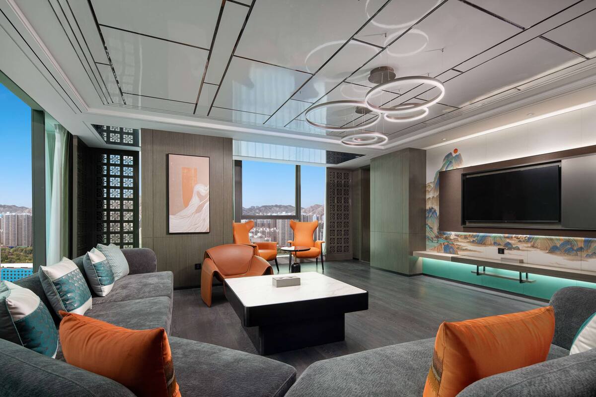 A modern living room with a large flat-screen TV, comfortable seating, and a city view.
