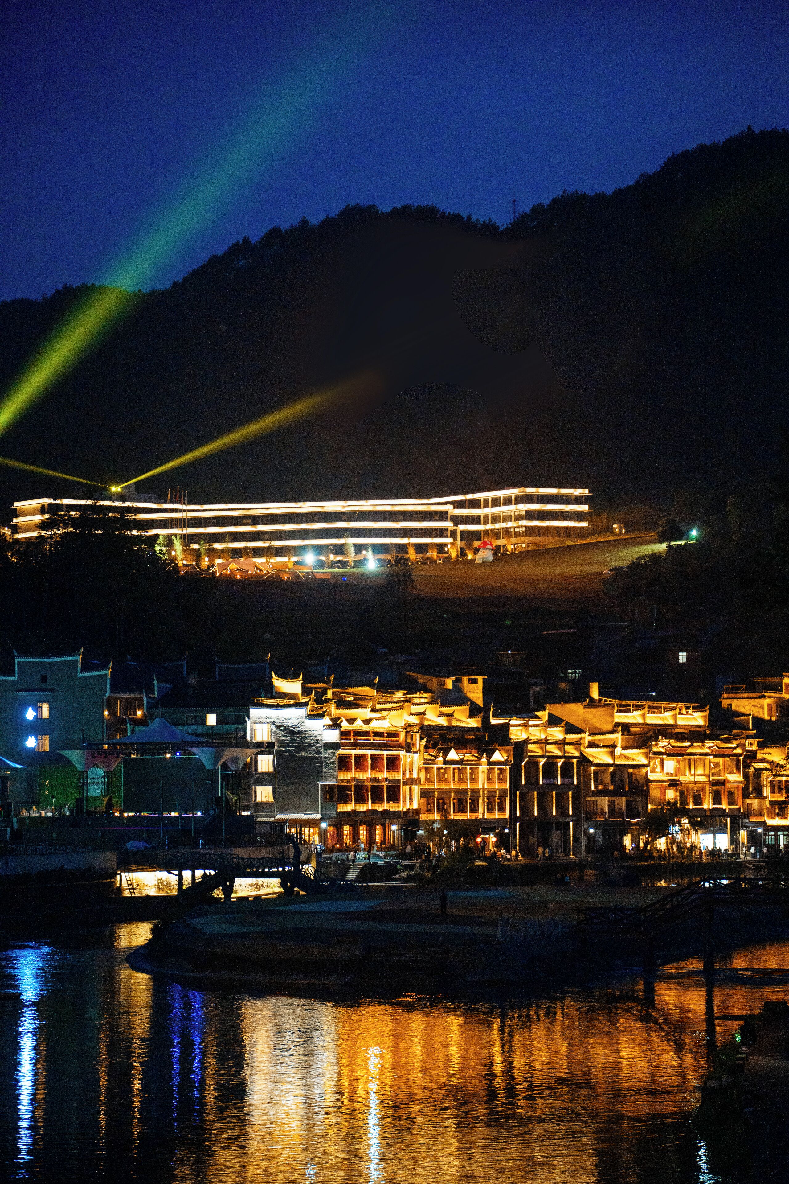 A waterfront hotel with illuminated buildings and a reflection on the water.