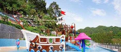 Un parque acuático con área de juegos temática de barco pirata, un tobogán y una piscina.