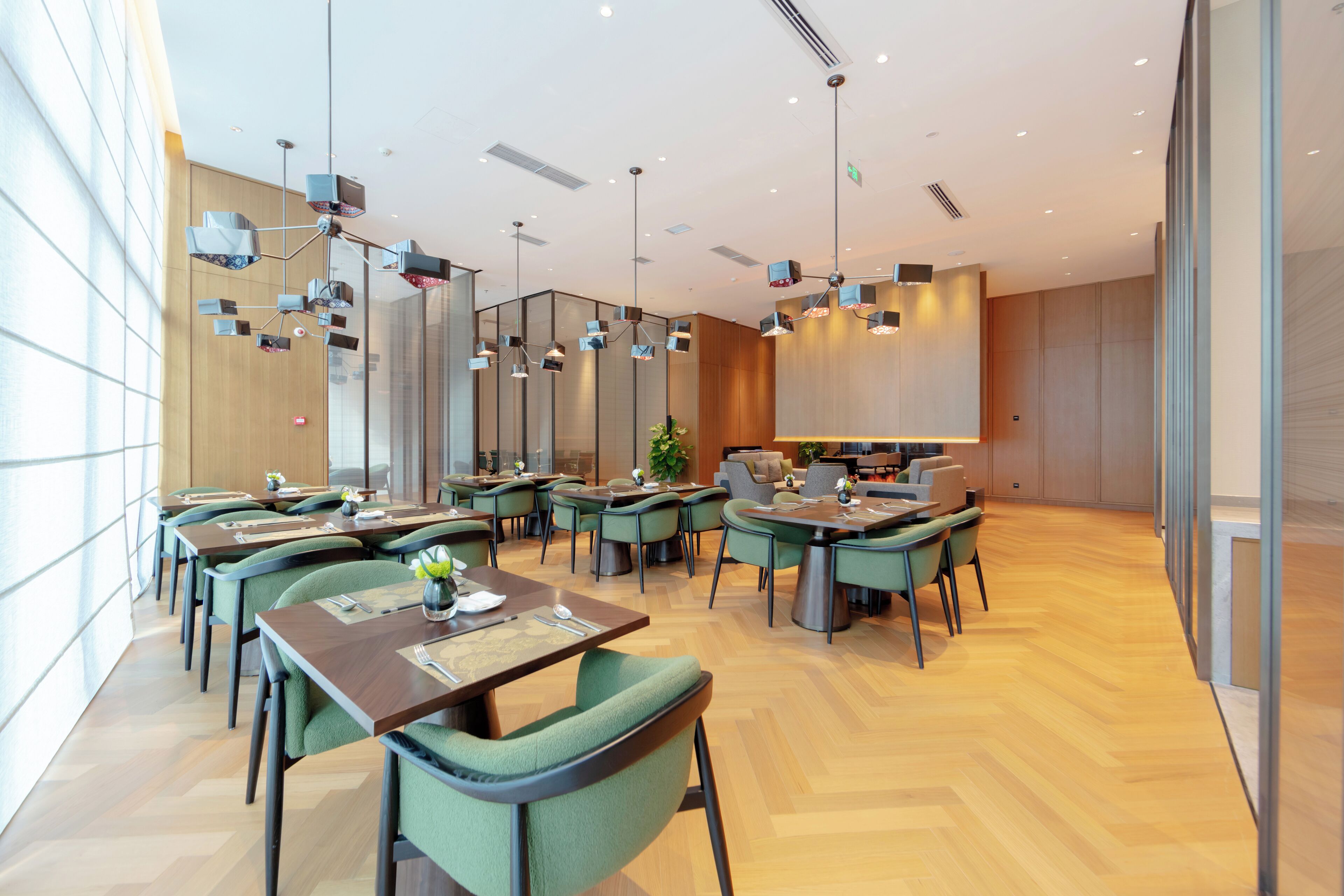 Un espace repas moderne doté de plusieurs tables et chaises, d’un plancher en bois et d’un éclairage suspendu.