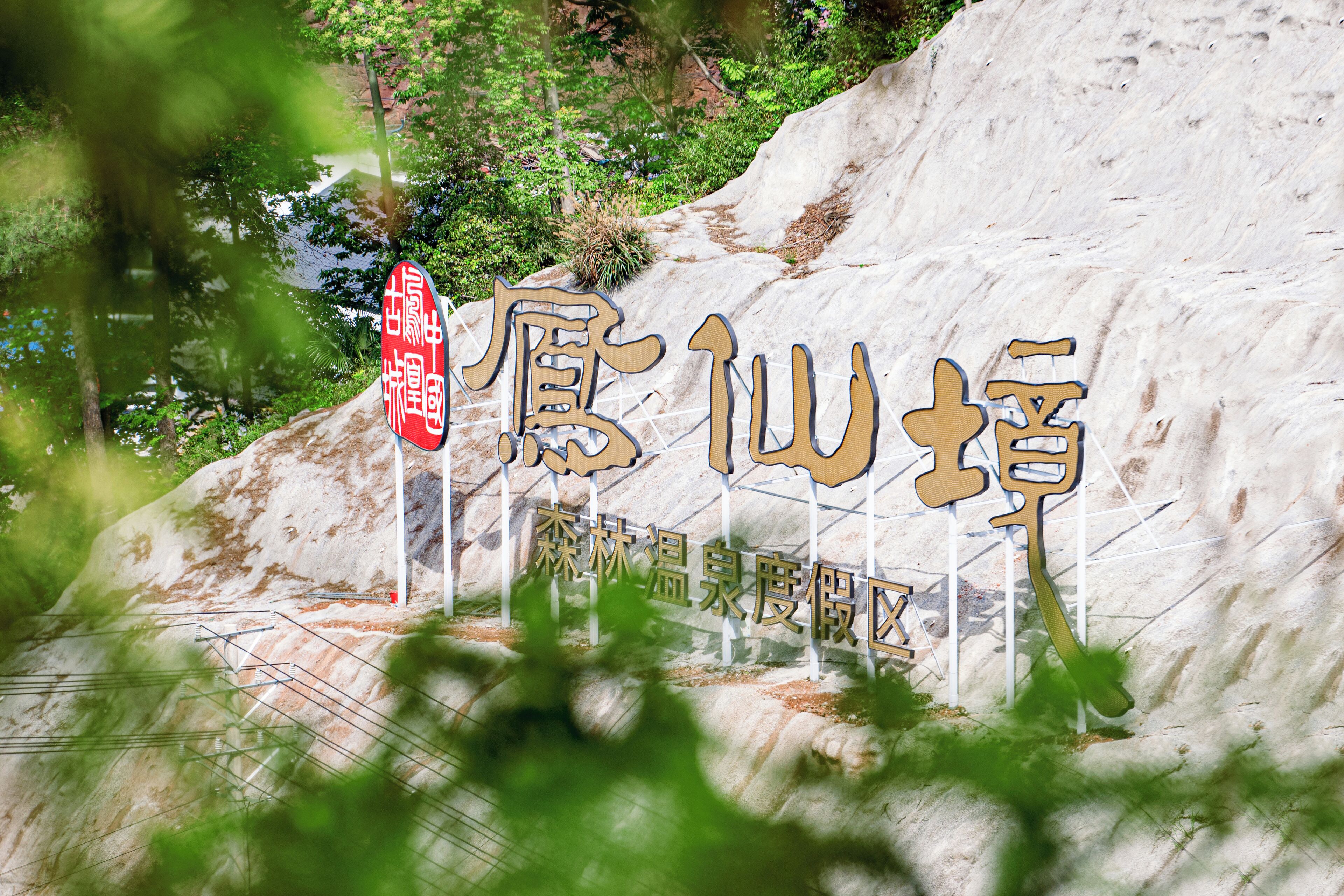 Ein großes Steinschild mit chinesischen Schriftzeichen, umgeben von Grünpflanzen und einer felsigen Landschaft.