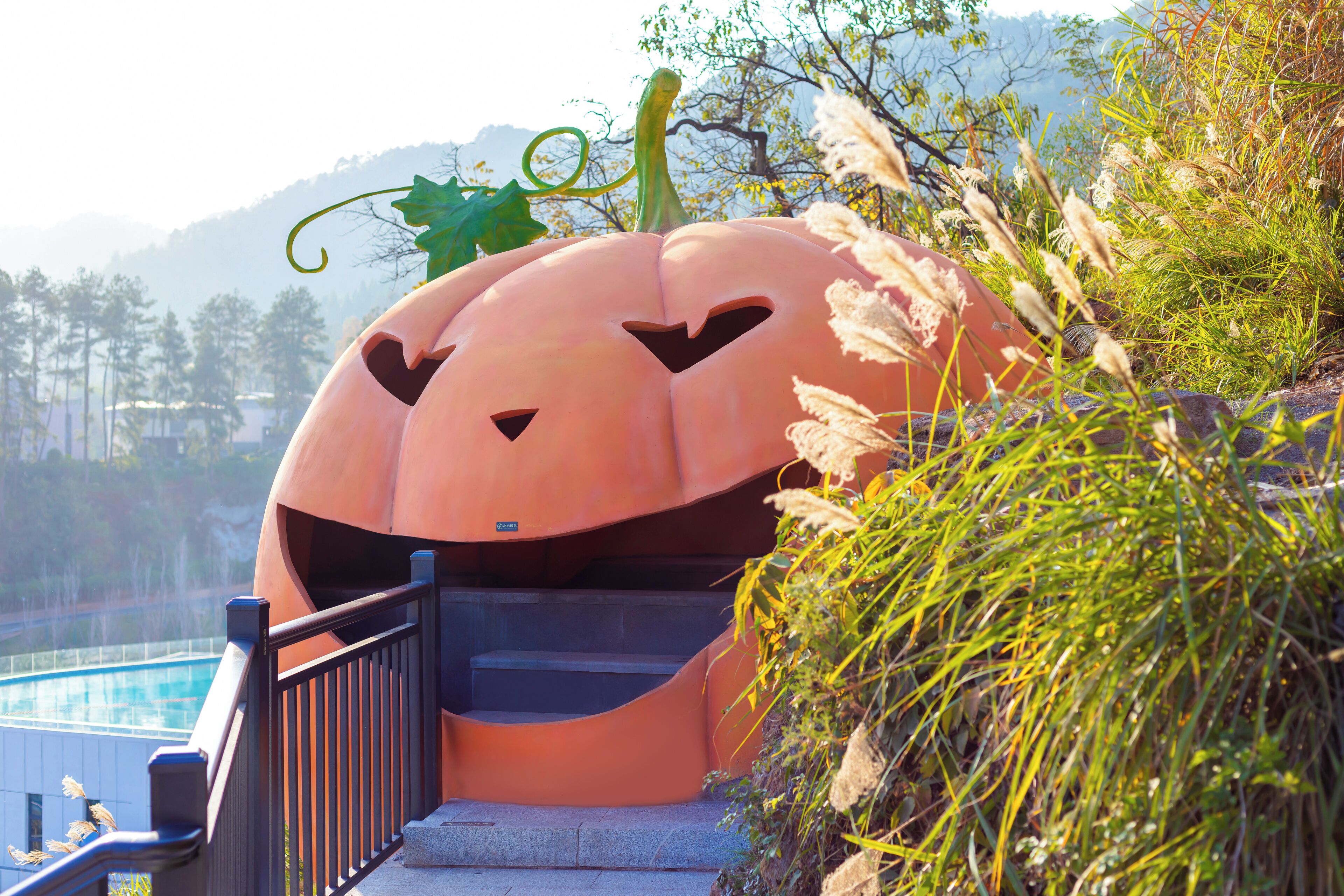 A large pumpkin-shaped structure with a staircase leading up to it, surrounded by greenery and a pool in the background.