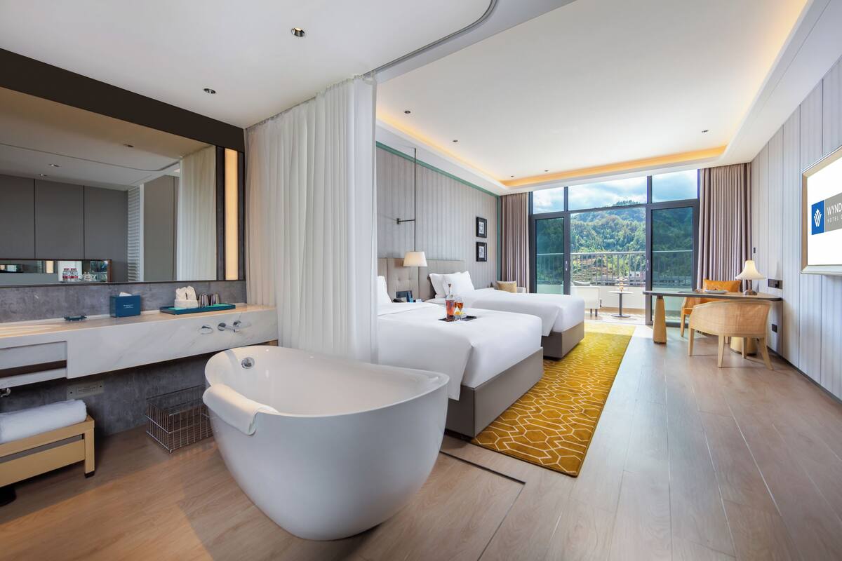 Habitación de hotel moderna con una bañera grande, cama, escritorio y vistas al exterior.