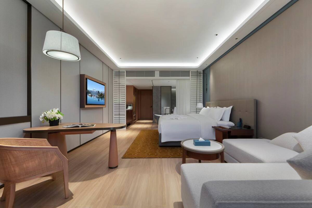 Una habitación de hotel moderna con una cama, mesitas de noche, un escritorio, una silla y una televisión.