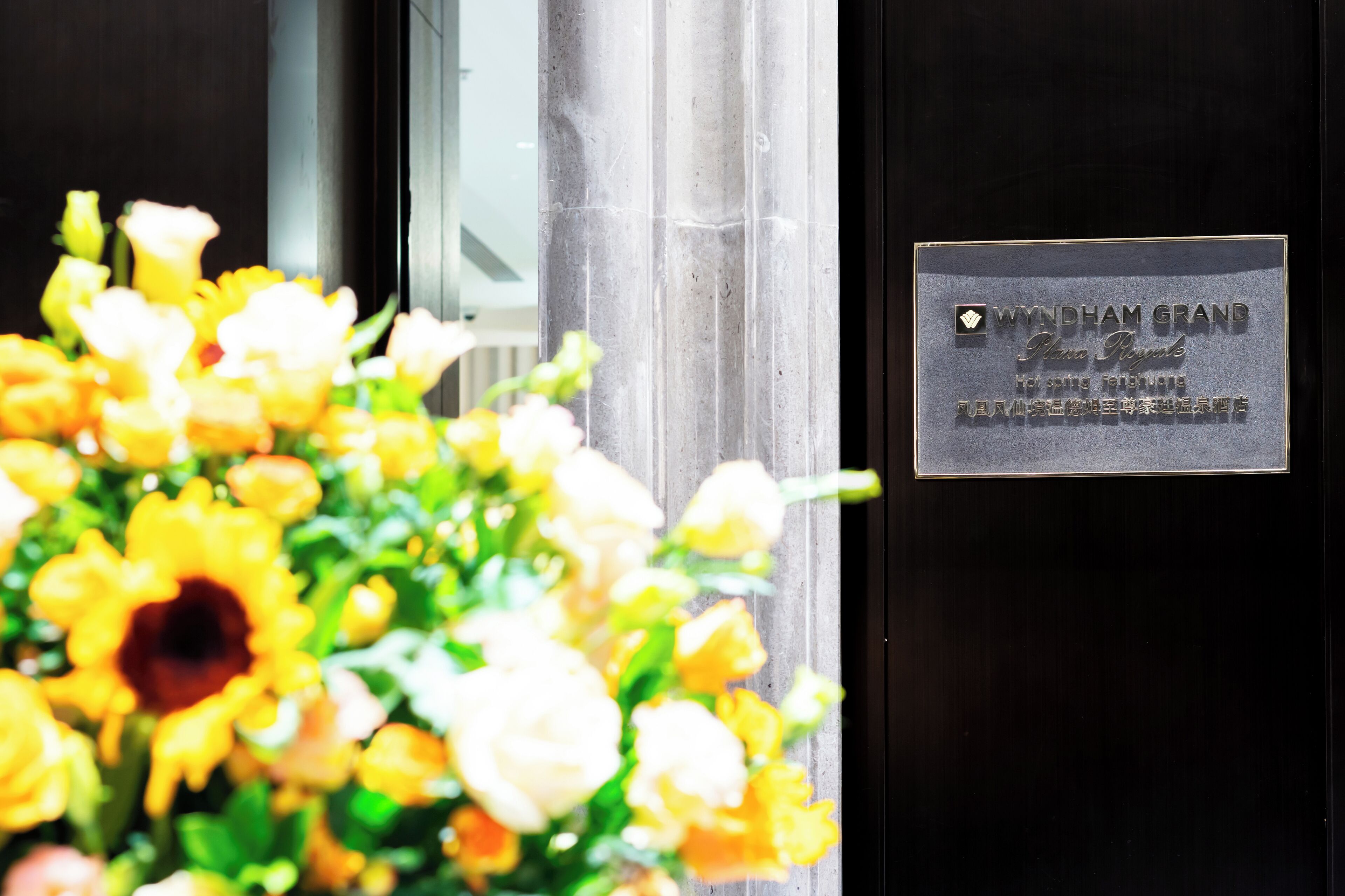Une plaque sur une porte, avec du texte, une colonne et une composition florale floue.