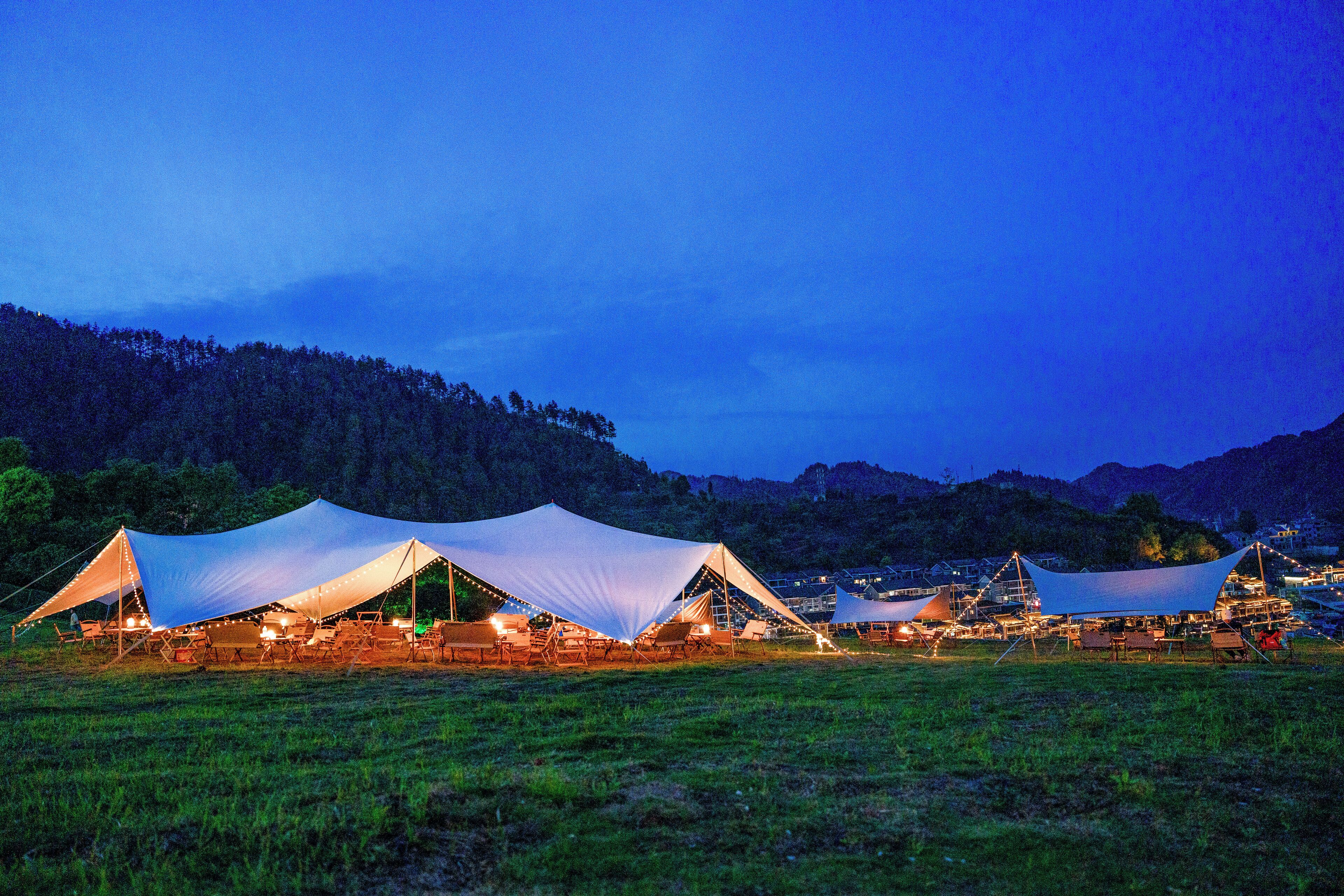 A series of tents set up in a grassy field with a mountainous backdrop.