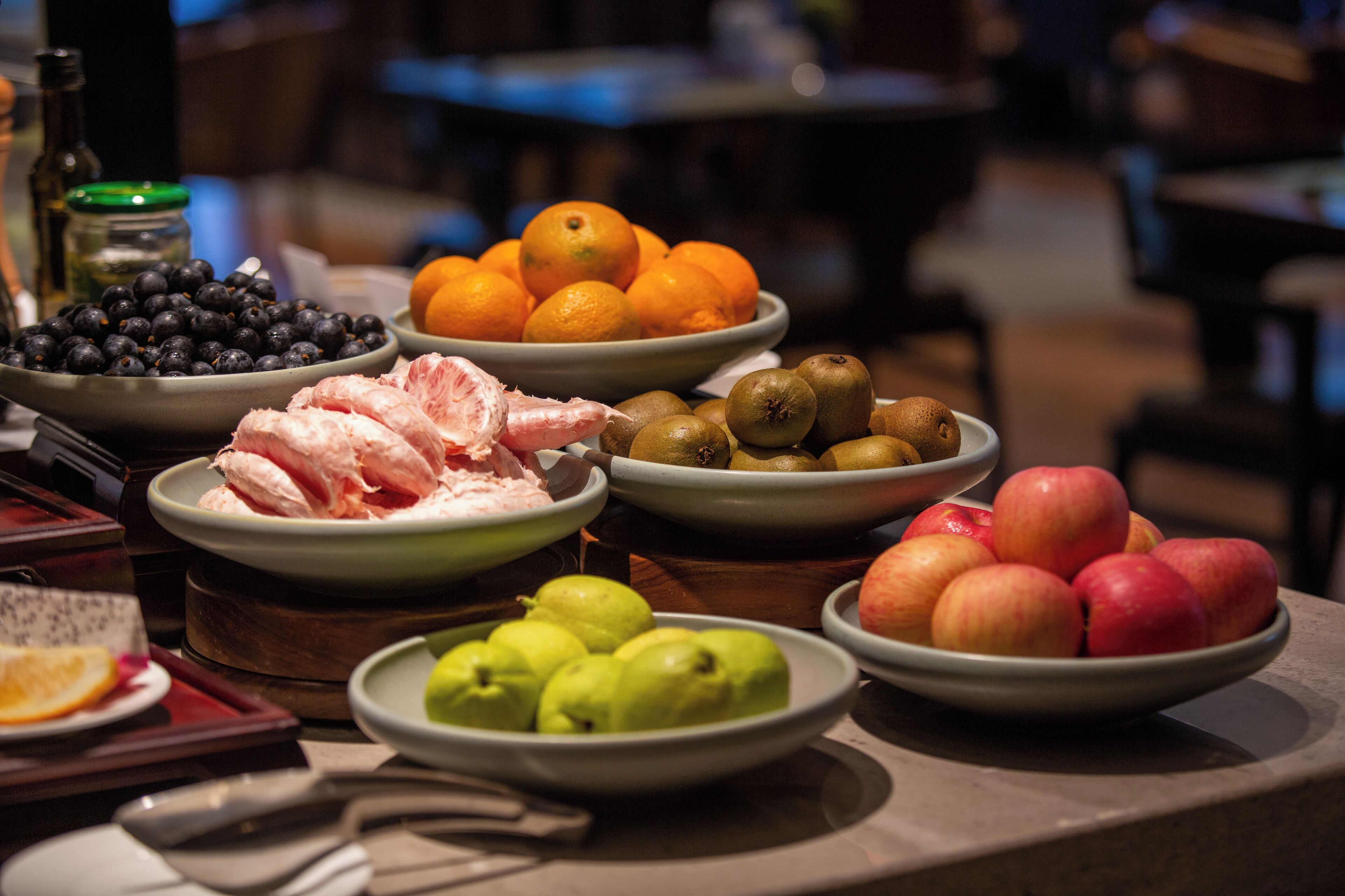 Een tafel met verschillende soorten fruit en groenten, zoals sinaasappels, appels en avocado's.
