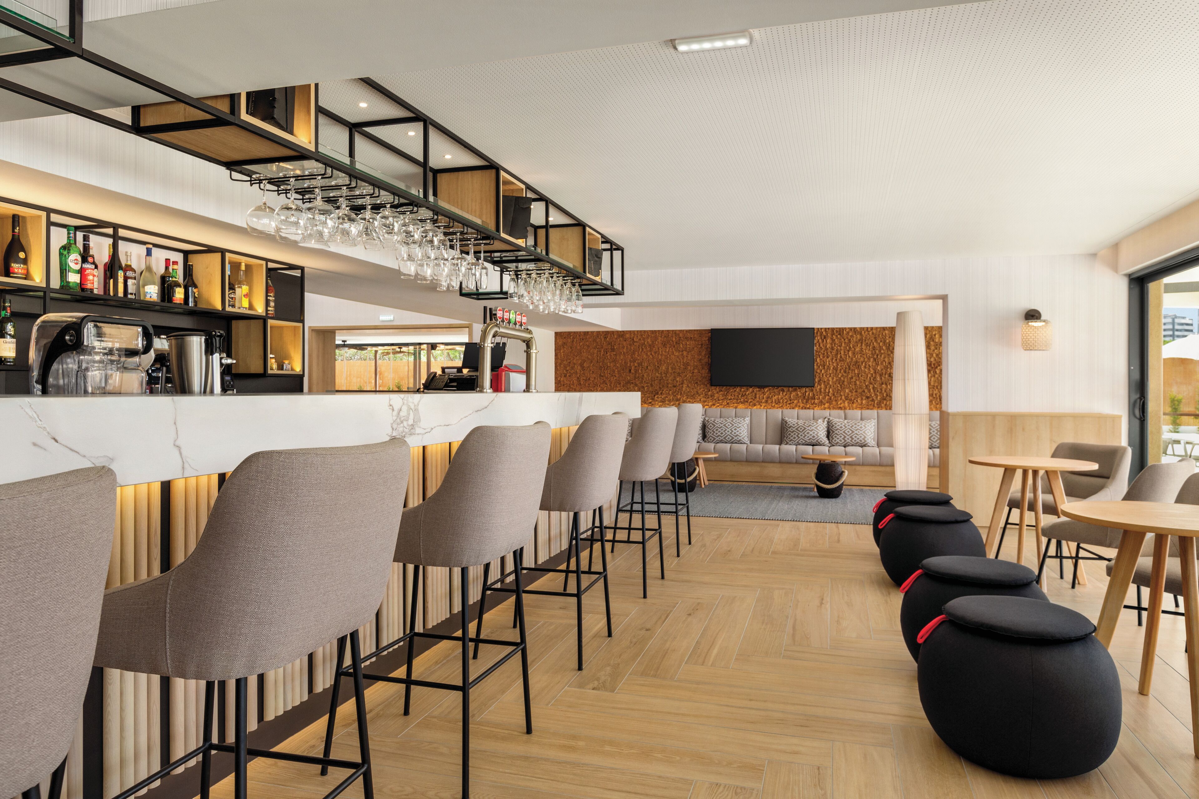 A modern bar area with high stools and a bar counter, a seating area with sofas, and a television mounted on the wall.