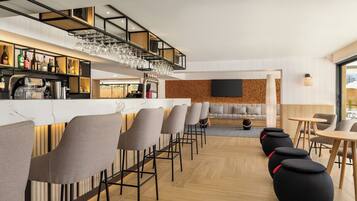 A modern bar area with high stools and a bar counter, a seating area with sofas, and a television mounted on the wall.