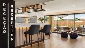 A reception area with a marble counter, two grey chairs, and a laptop. There are tables and chairs outside with umbrellas. - Wyndham Residences Alvor Beach (Portimão)