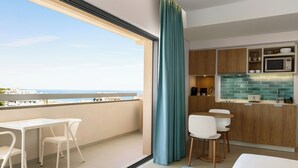 A modern kitchen with a view of the sea, a balcony with a table and chairs, and a large window with curtains. - Wyndham Residences Alvor Beach (Portimão)