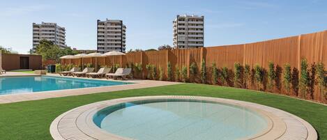 A swimming pool with a wooden deck, surrounded by a well-manicured lawn and lounge chairs.