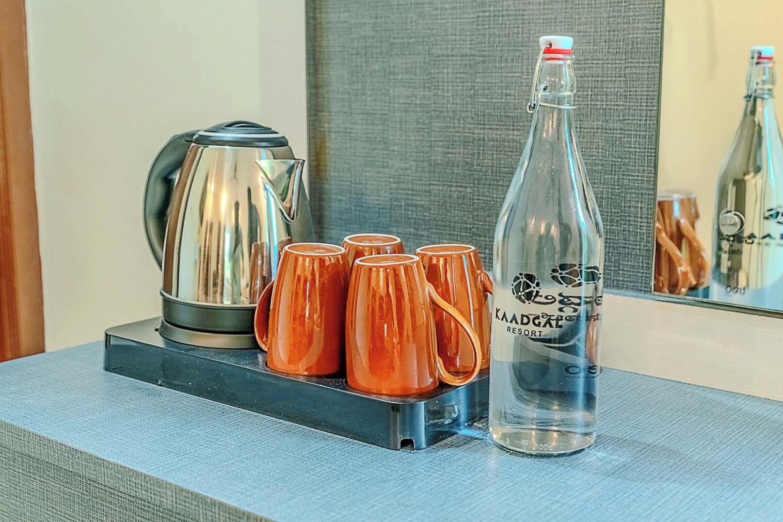 Una mesa con una tetera, cuatro tazas naranjas y una botella de agua.