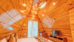 A cozy, wooden-paneled room with a bed, a TV, and a window with curtains.