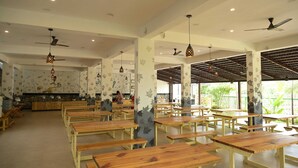 A spacious indoor dining area with wooden tables and benches, ceiling fans, and decorative wall art.