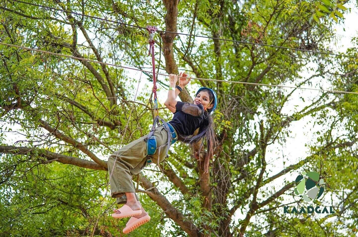 Una persona che pratica un'attività all'aperto, sospesa tra gli alberi con imbracature e corde di sicurezza.