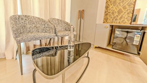 A dining area with a glass table and two patterned chairs, a refrigerator, and a patterned wall.
