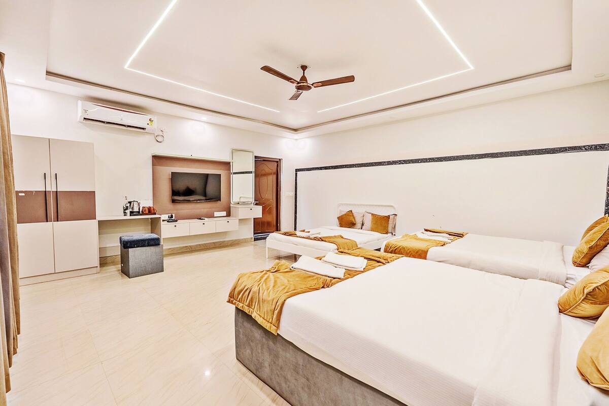 Une chambre d’hôtel avec un grand lit, un lit plus petit, une télévision, une armoire et un ventilateur de plafond.