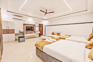 Habitación de hotel con una cama grande, una cama más pequeña, un televisor, un armario y un ventilador de techo.