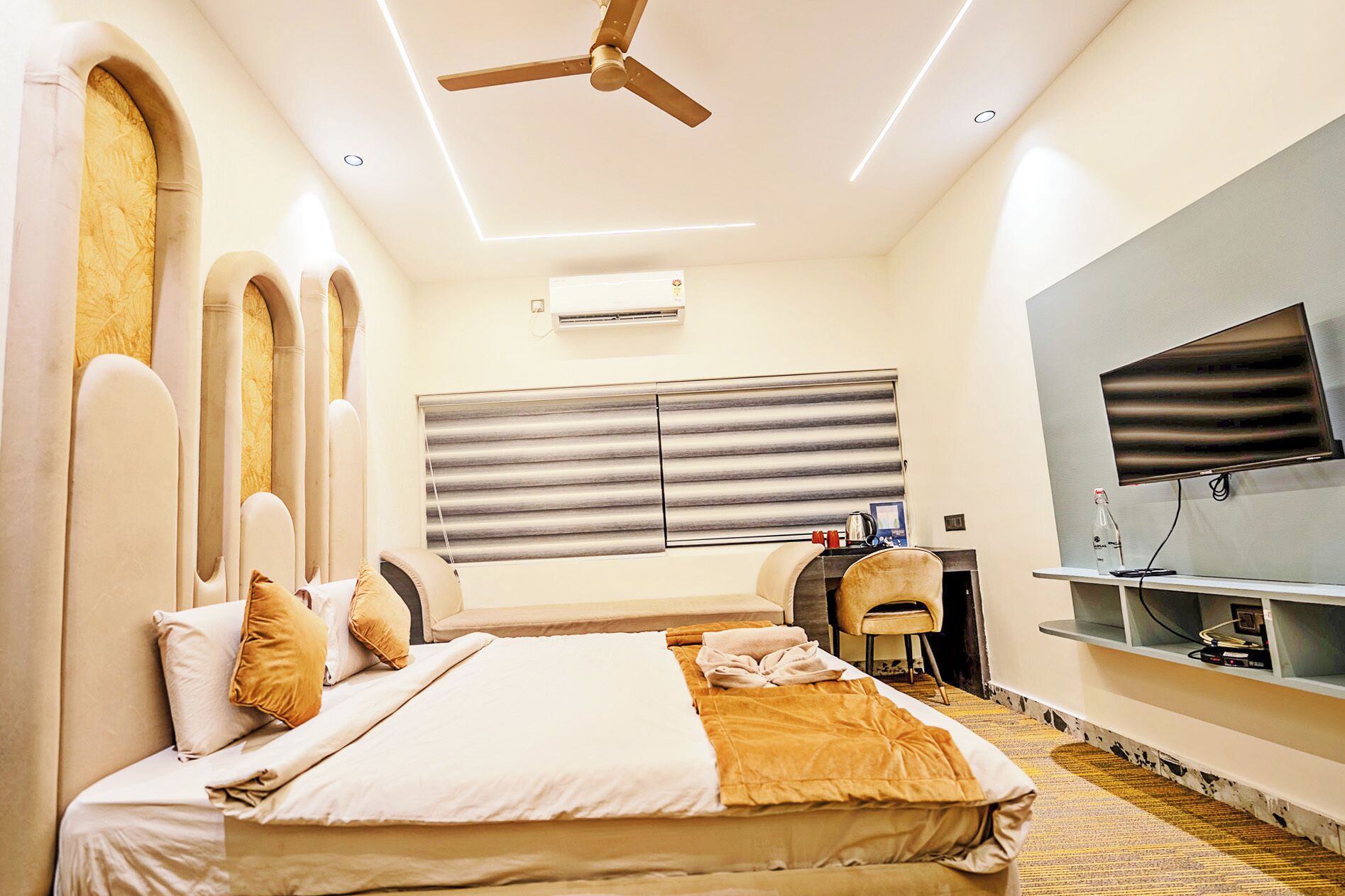 A modern hotel room with a large bed, a ceiling fan, a flat-screen TV, and a desk with a chair.