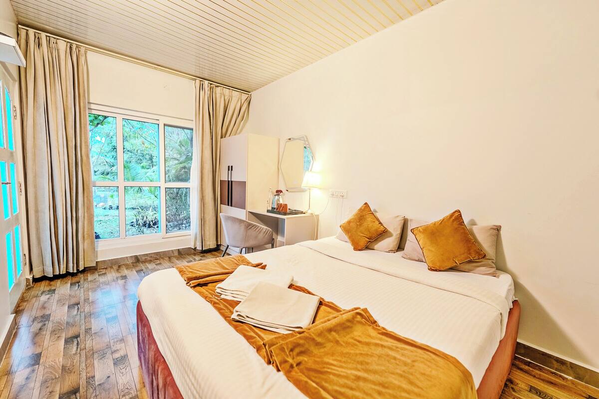 Une chambre d’hôtel avec un grand lit, un bureau, une chaise et une fenêtre avec des rideaux.