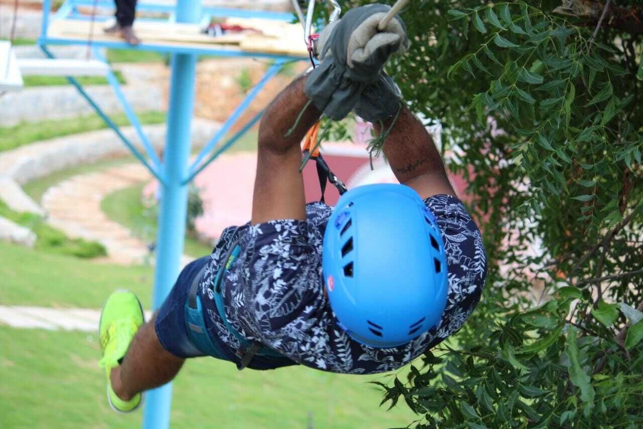 A person in a blue helmet and patterned shorts climbing a blue structure outdoors.