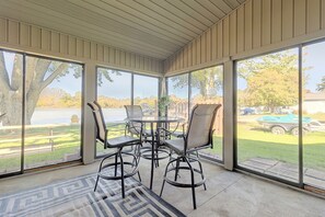A covered patio with a table and chairs, large windows, and a view of a lake and trees.