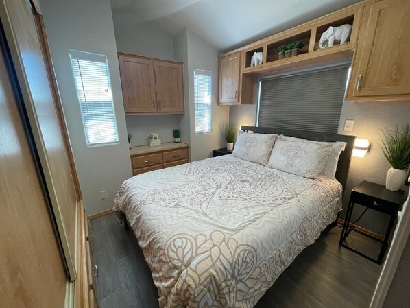 A compact bedroom with a bed, bedside tables, a small desk, and built-in wooden cabinets.