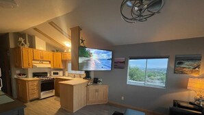 A modern kitchen with wooden cabinets, a built-in microwave, and a large TV. - Elephant Lake Sunset Oasis (Elephant Butte)