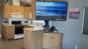 A modern kitchen with wooden cabinets, a built-in oven, microwave, and coffee maker. A flat-screen TV is mounted on the wall displaying a beach scene. - Elephant Lake Sunset Oasis (Elephant Butte)