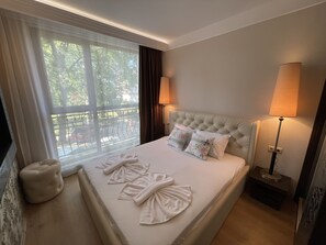 Relax in comfort with a large bed featuring a tufted headboard, two pillows, and a bedside view of lush greenery.