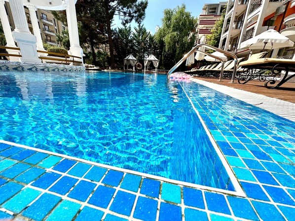 Relax by the pool surrounded by lounge chairs and umbrellas, with a beautiful view of the surrounding buildings and lush greenery.