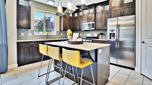 A modern kitchen with dark wood cabinets, stainless steel appliances, and a central island with yellow bar stools. - Entrada at Moab 420 and 424 (Moab)