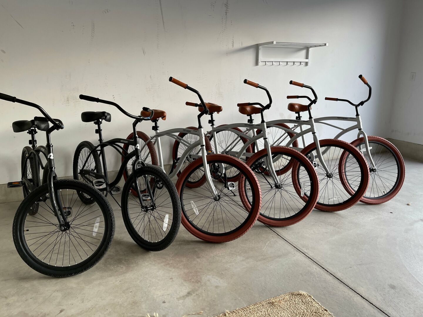 Une rangée de vélos aux couleurs et aux designs de guidon différents, garés à l’intérieur contre un mur uni.