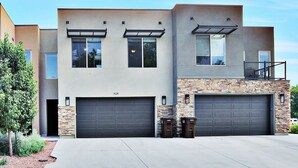 A modern two-story house with a stone facade, two garage doors, and a small balcony with outdoor furniture. - Entrada at Moab 420 and 424 (Moab)
