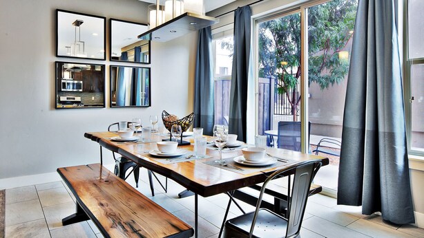 A dining area with a wooden table set for four, a bench, and a view of a garden through large windows. - Entrada at Moab 420 and 424 (Moab)