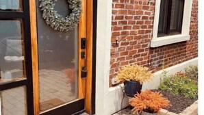 A brick building with a wooden door, a wreath, and a doormat with the text "Only Good Vibes".