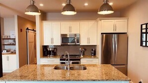 A modern kitchen with granite countertops, stainless steel appliances, and pendant lighting.