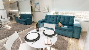 Una sala de estar moderna con un sofá azul verdoso, una mesa de comedor dispuesta con platos, cubiertos y una botella de vino.