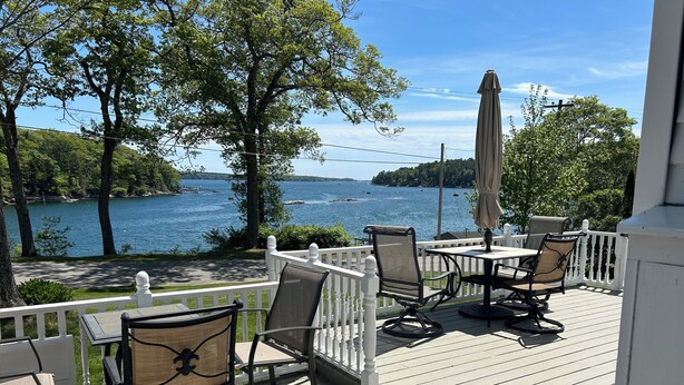En terrasse med udendørs siddepladser med udsigt over en sø med både og en bro.