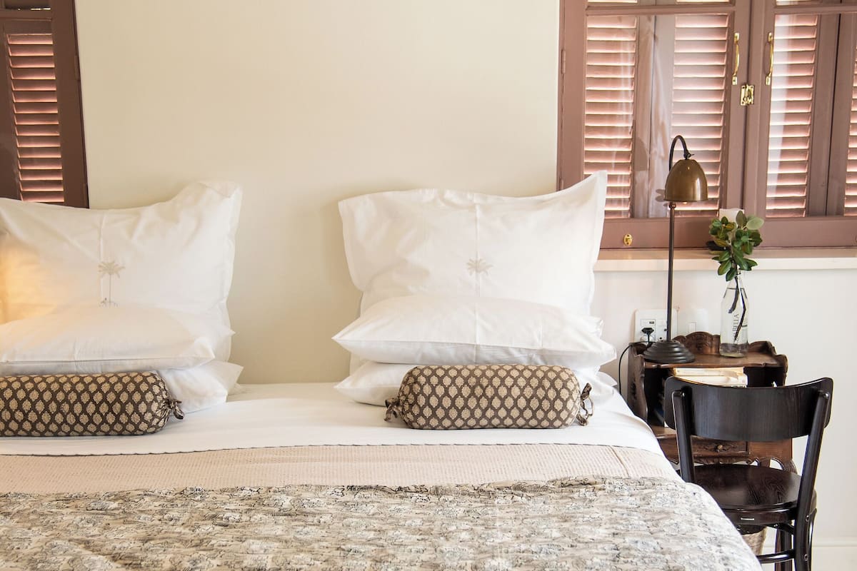 A bedroom with a bed, two bedside tables, a chair, and a window with shutters.