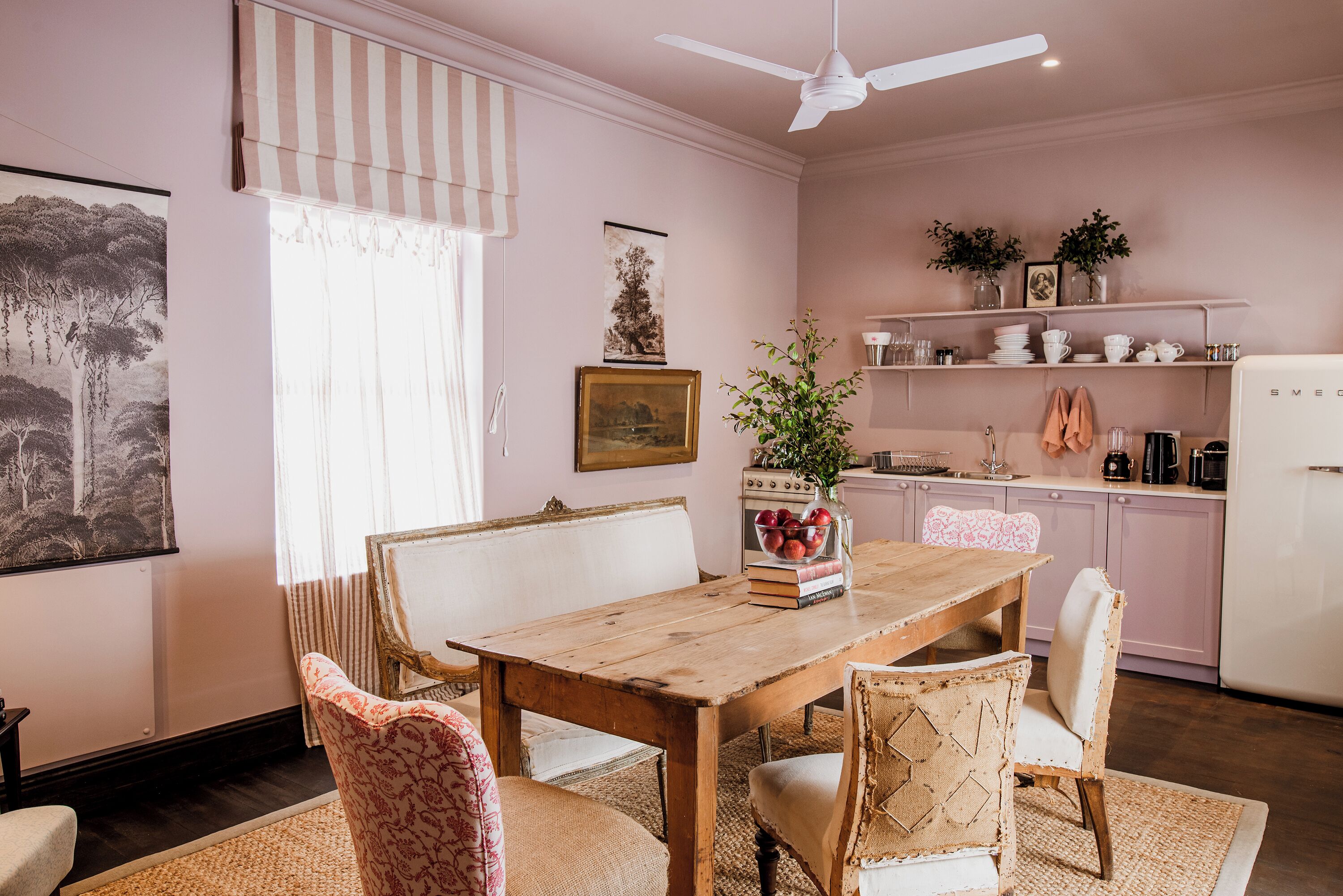 A dining area with a wooden table and chairs, a ceiling fan, and a kitchen in the background.